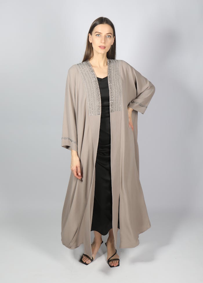 Stylish woman in an abaya posing confidently indoors with a simple white background.